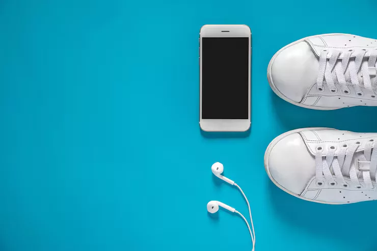 Flatlay PNG of sneakers, a phone and earbuds before background removal, arranged on a blue board